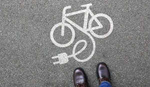 E-Bike-Symbol auf der Straße mit Kreide aufgezeichnet vor einem Paar Füße