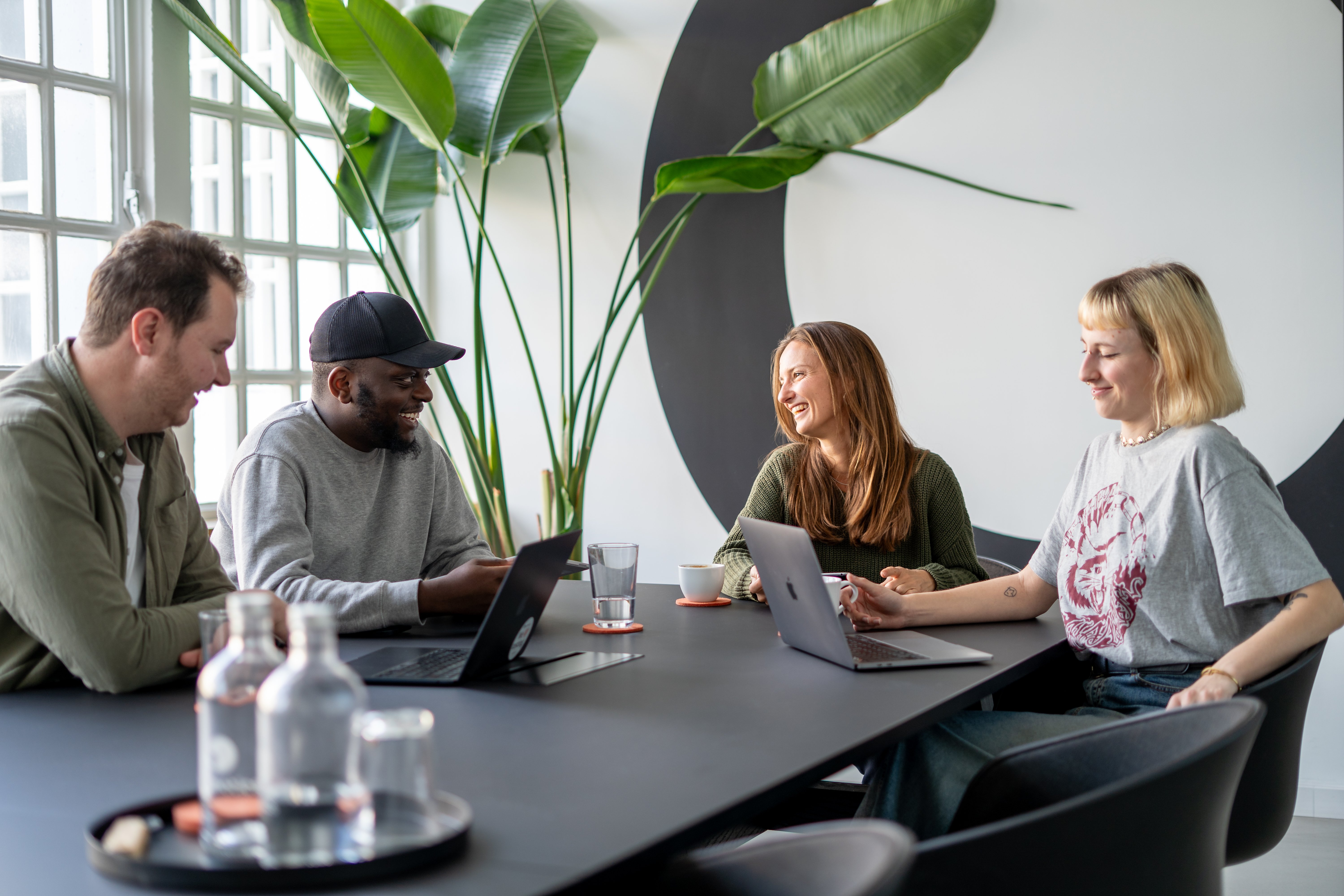 Vier Personen lachend an einem Konferenztisch mit Laptops vor sich