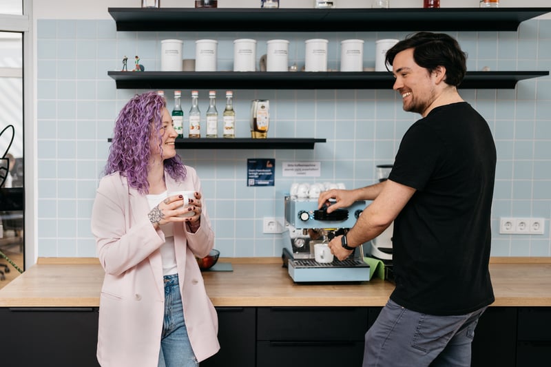 Ein Mann unterhält sich mit seiner Kollegin, während er sich einen Kaffee macht. 